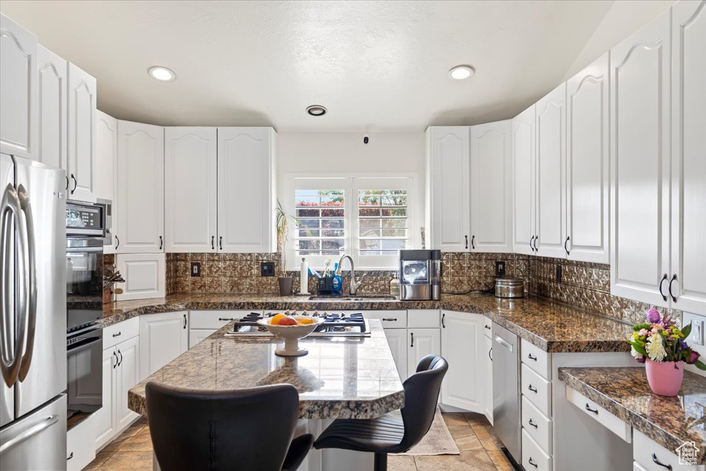 Kitchen featuring a sink, appliances with stainless steel finishes, white cabinets, and tasteful backsplash