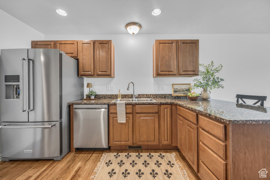 Kitchen featuring a sink, appliances with stainless steel finishes, brown cabinetry, and a peninsula