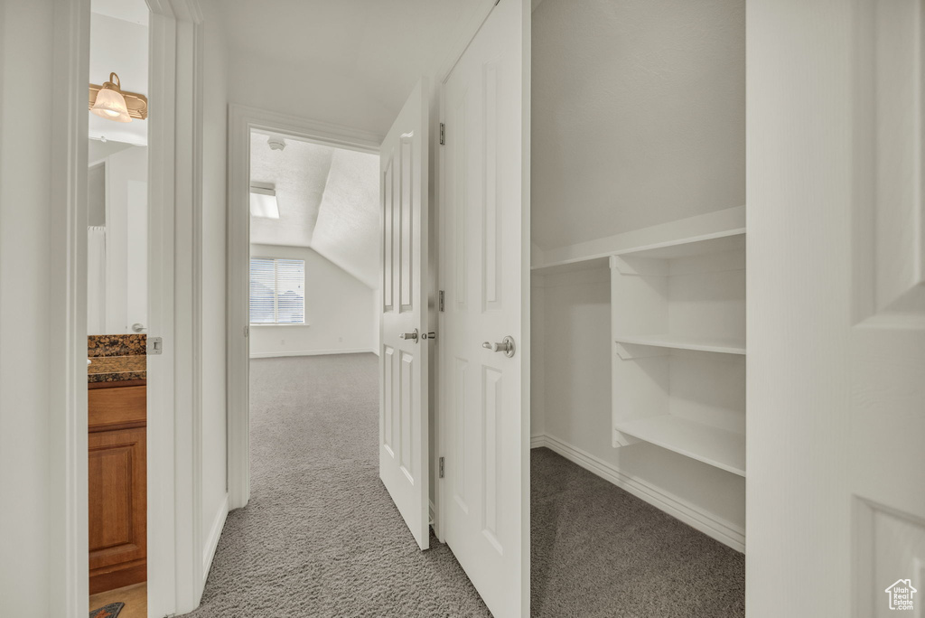 Corridor featuring baseboards, carpet, and vaulted ceiling