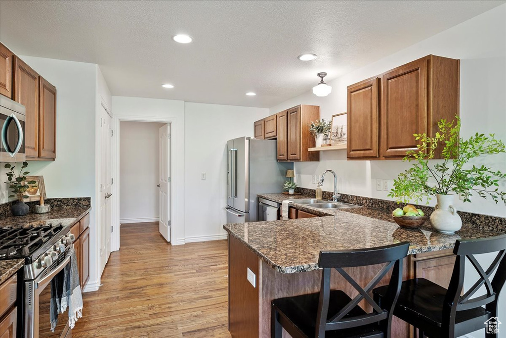 Kitchen featuring stainless steel appliances, a sink, a kitchen bar, brown cabinetry, and light wood finished floors
