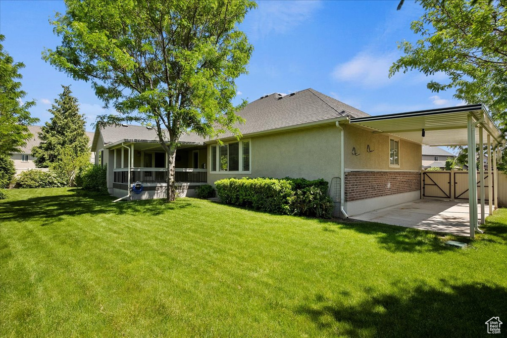 Back of house with a gate, a lawn, brick siding, and stucco siding