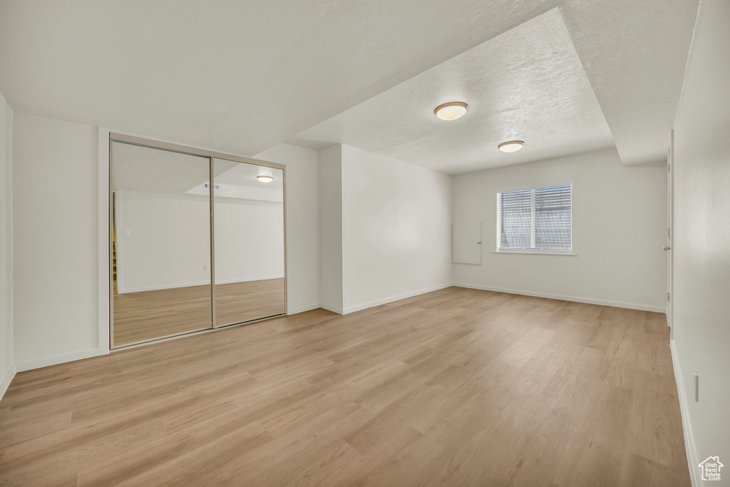 Unfurnished bedroom featuring a textured ceiling, baseboards, light wood-style flooring, and a closet