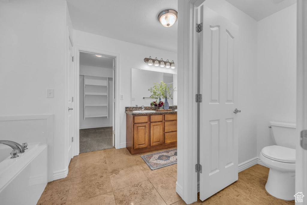 Bathroom with vanity, baseboards, a garden tub, and toilet