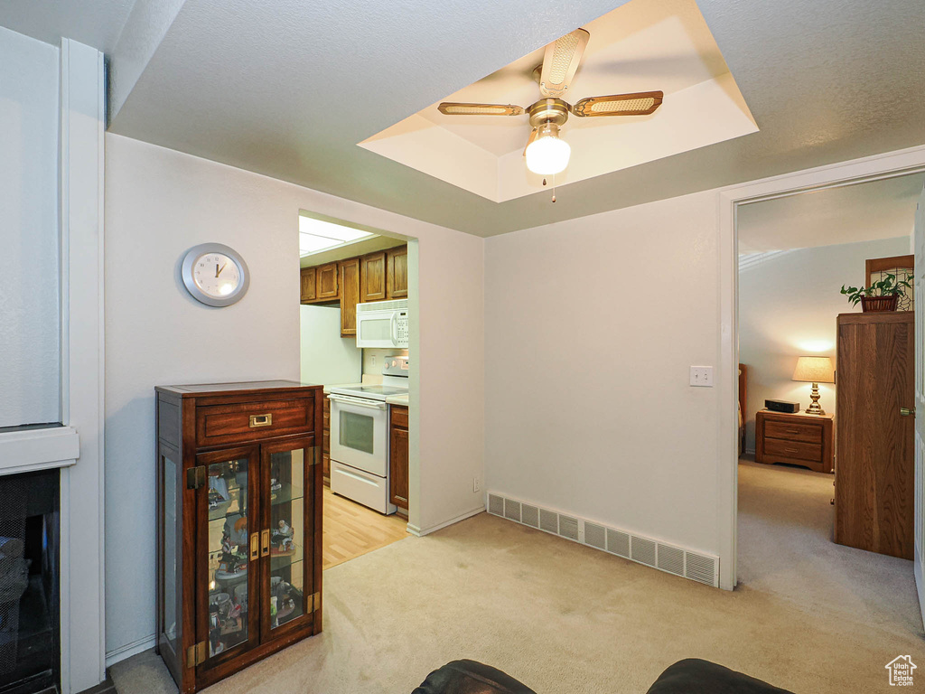 Interior space with visible vents, a ceiling fan, a tray ceiling, and light carpet