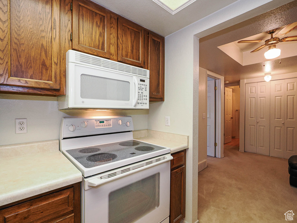 Kitchen featuring a ceiling fan, brown cabinets, light countertops, light carpet, and white appliances