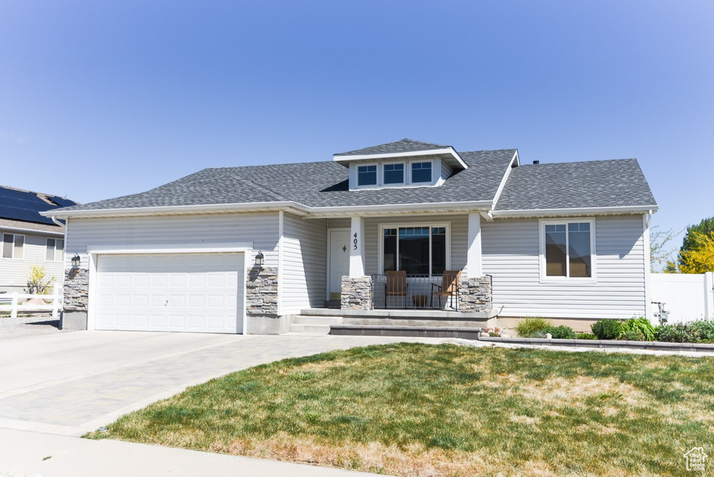 View of front facade with a garage, fence, covered porch, a front yard, and driveway
