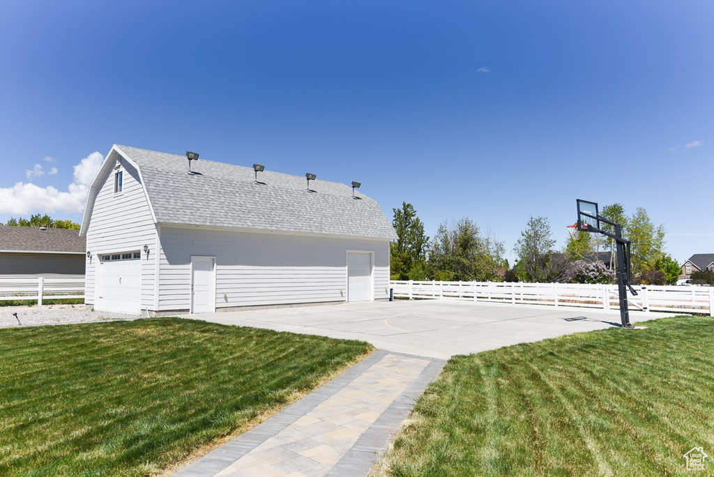 View of property exterior featuring a lawn, a garage, roof with shingles, and fence