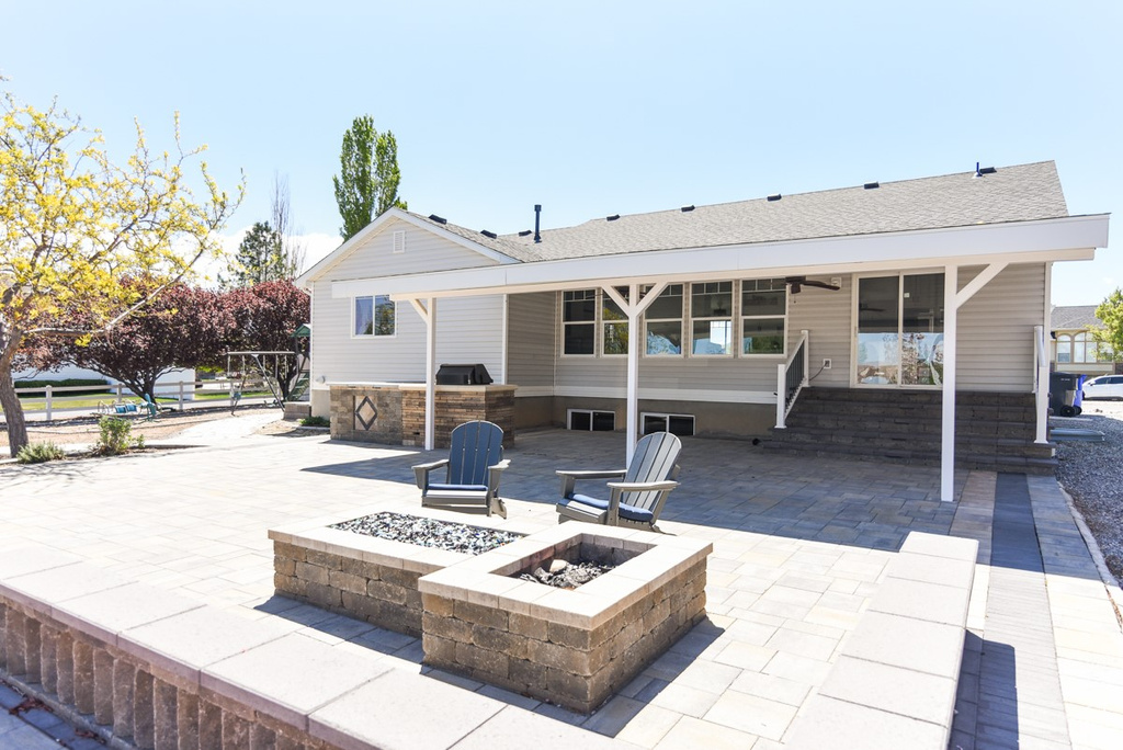 Rear view of property with a shingled roof, an outdoor fire pit, and a patio area