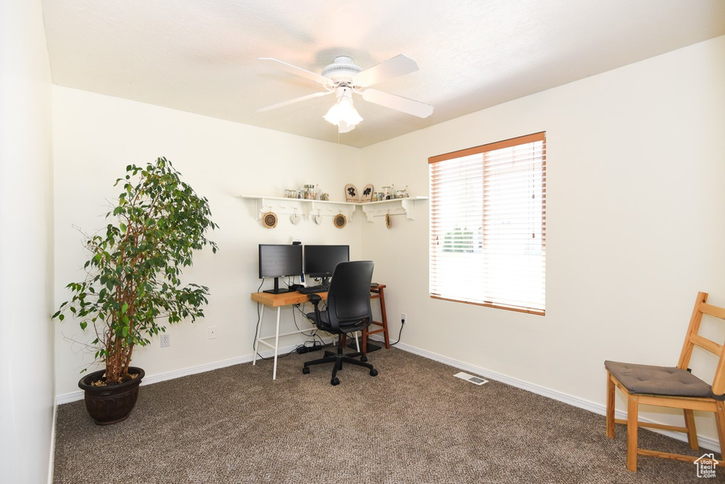 Carpeted office space with visible vents, baseboards, and ceiling fan