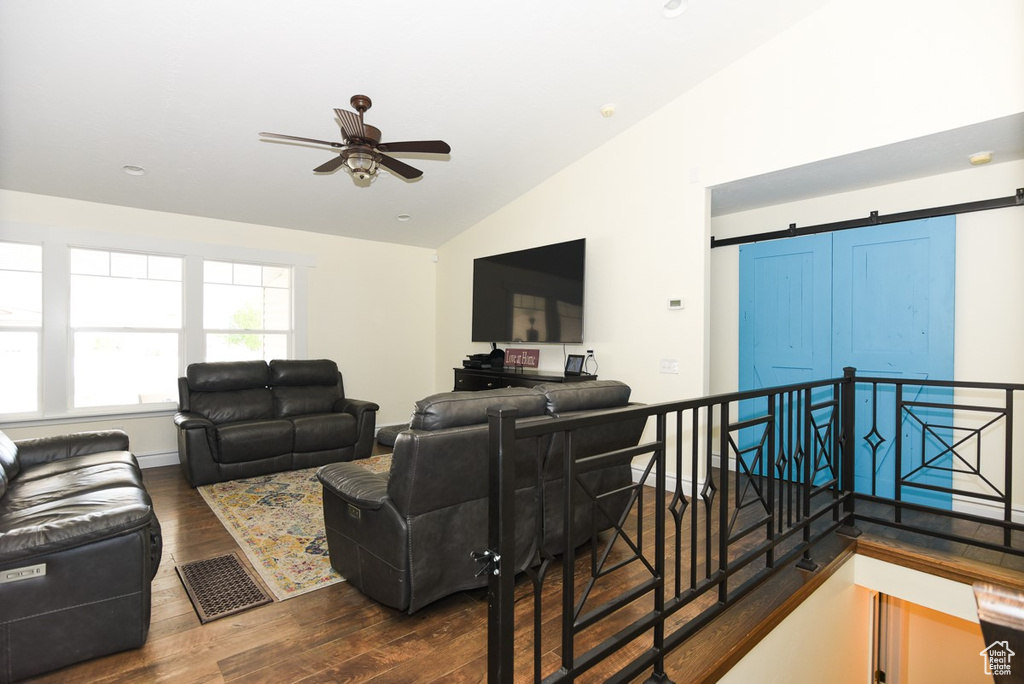 Living area featuring visible vents, ceiling fan, a barn door, dark wood finished floors, and vaulted ceiling
