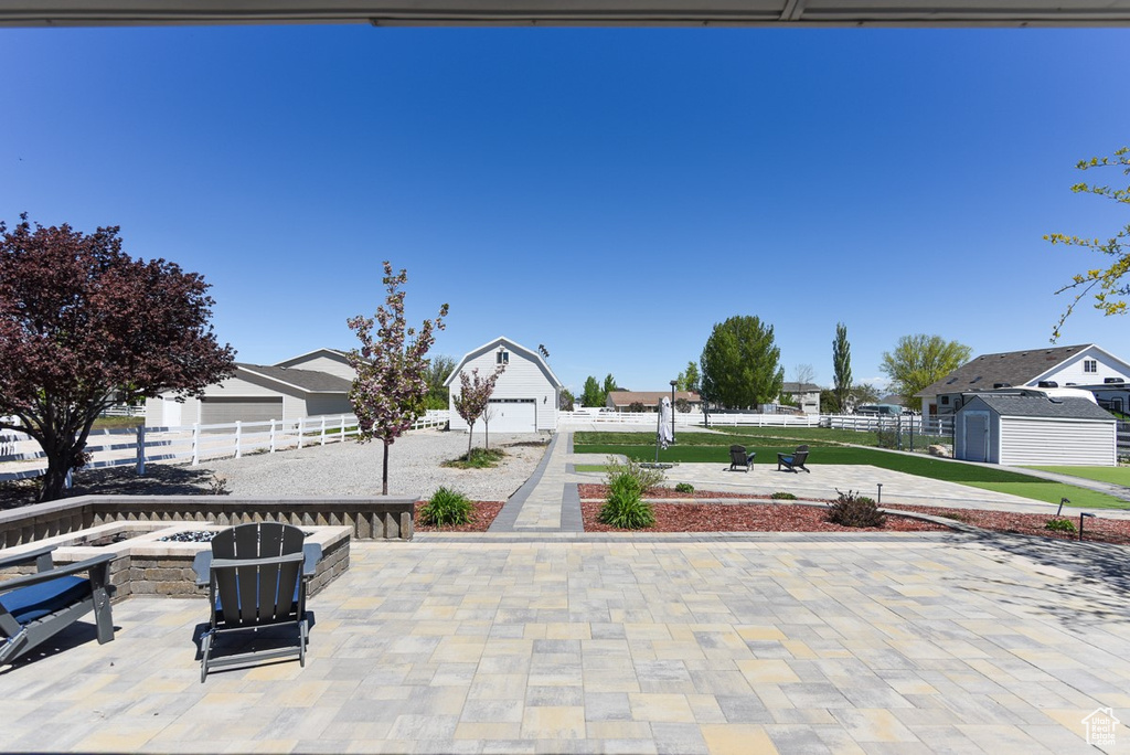 View of patio / terrace with a garage, fence, an outdoor fire pit, an outbuilding, and a residential view