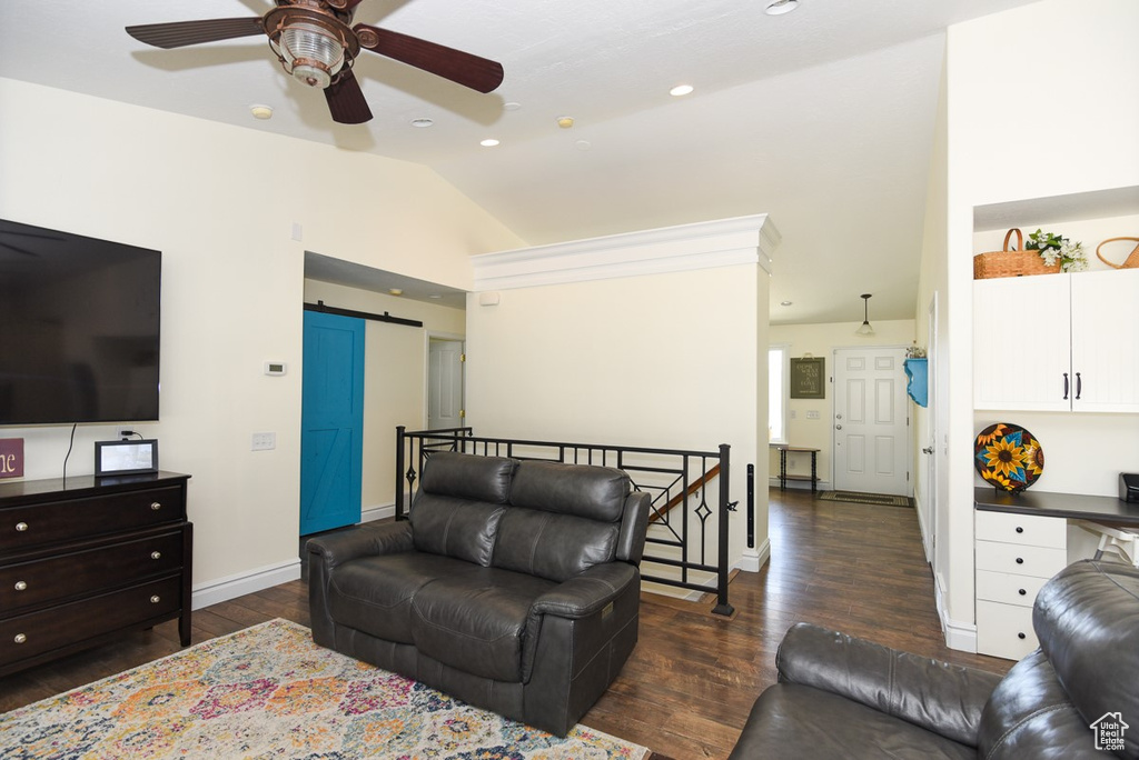 Living area featuring baseboards, dark wood-type flooring, a barn door, a ceiling fan, and vaulted ceiling