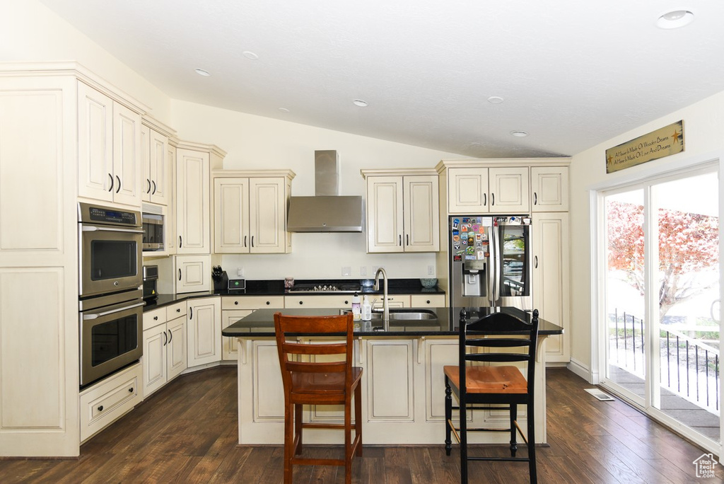 Kitchen with a sink, wall chimney exhaust hood, appliances with stainless steel finishes, and cream cabinets