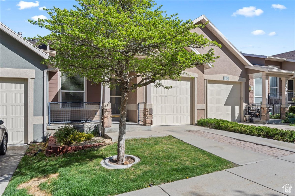 View of front of house featuring an attached garage, a front lawn, stucco siding, and concrete driveway