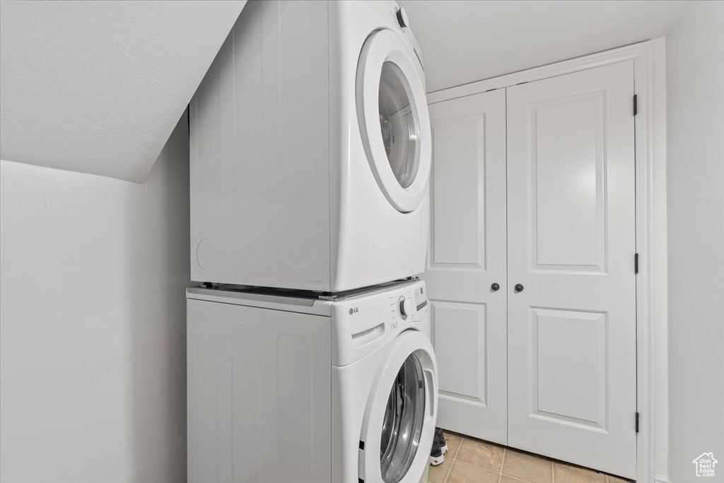 Washroom with a textured ceiling, stacked washer / drying machine, and light tile patterned floors