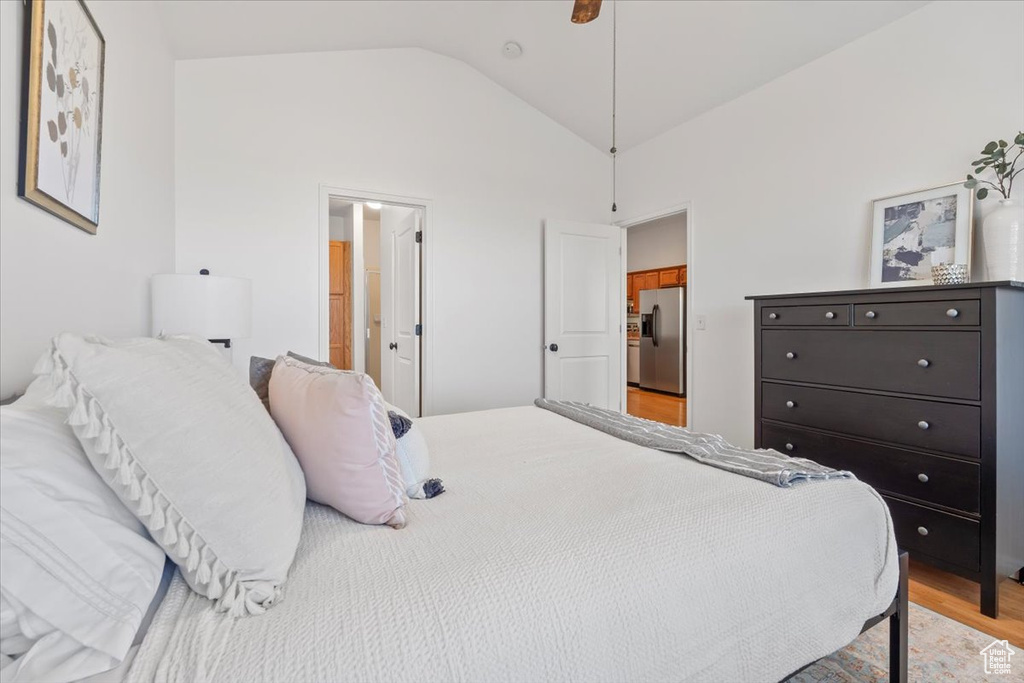 Bedroom with stainless steel fridge, light wood finished floors, and lofted ceiling
