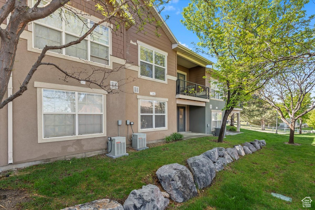 Back of house with stucco siding, central air condition unit, a yard, and a balcony