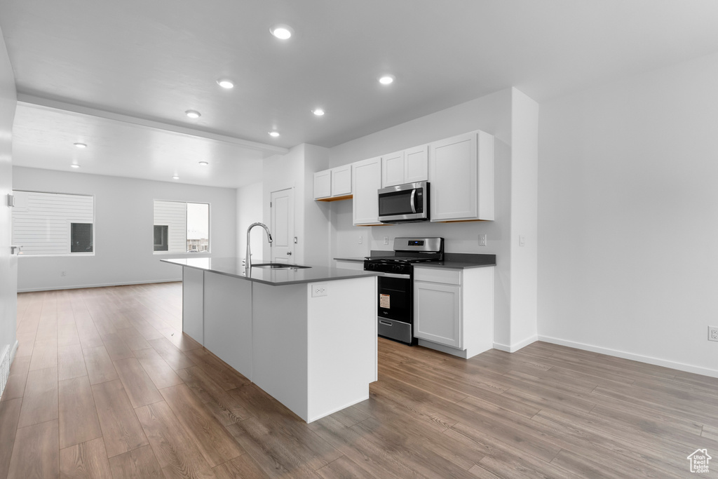 Kitchen featuring appliances with stainless steel finishes, dark countertops, a sink, light wood finished floors, and open floor plan