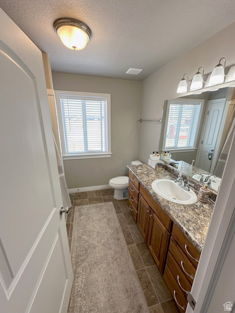 Bathroom with tile flooring, vanity, toilet, and a textured ceiling