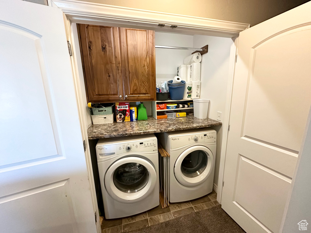 Laundry room featuring washing machine and clothes dryer, cabinet space, and dark tile patterned flooring