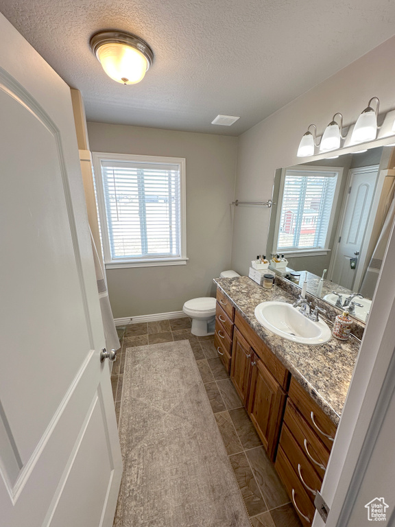 Bathroom featuring vanity, toilet, healthy amount of natural light, a textured ceiling, and baseboards