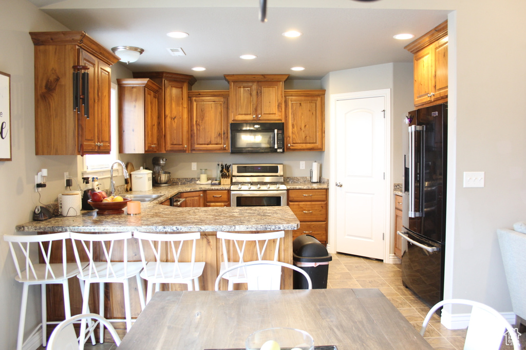 Kitchen featuring black appliances, a sink, a peninsula, recessed lighting, and light countertops