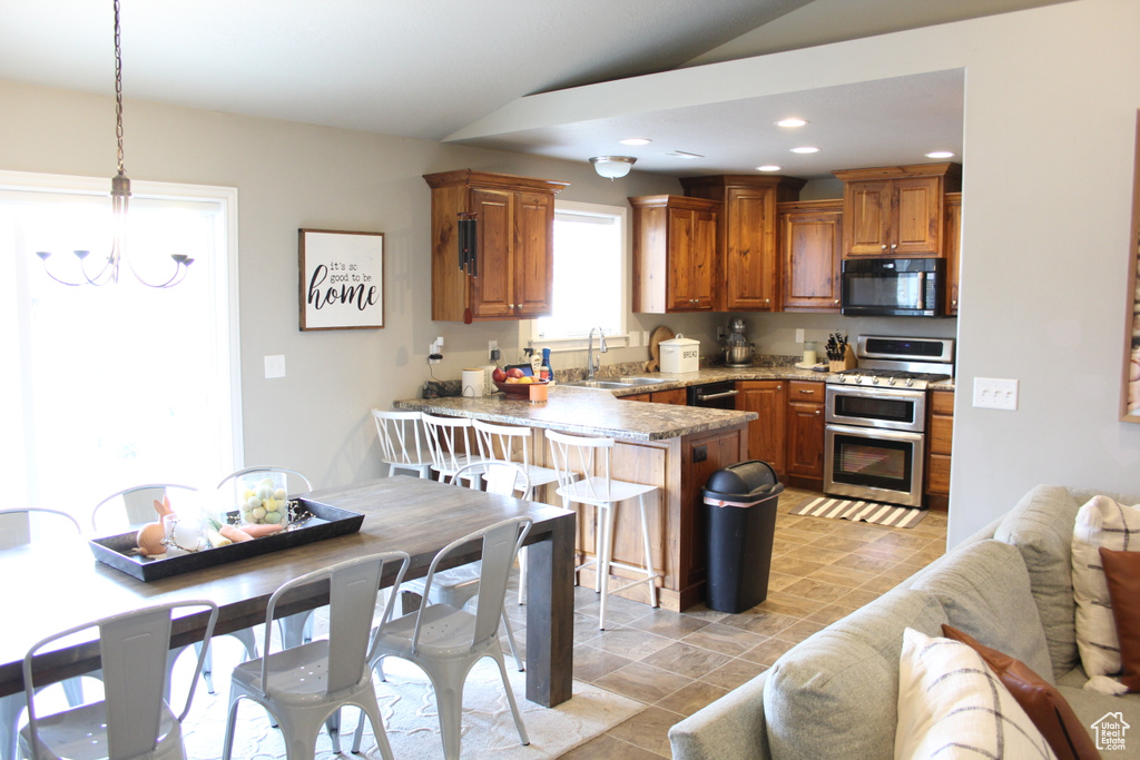 Kitchen featuring black appliances, a sink, a peninsula, lofted ceiling, and brown cabinetry
