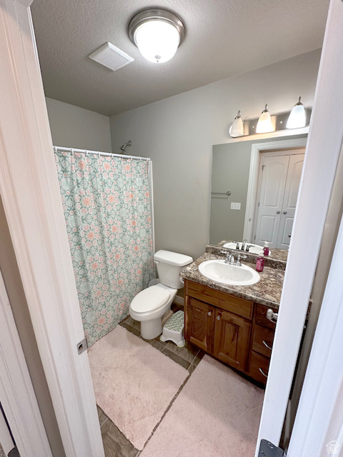 Bathroom with oversized vanity, toilet, tile floors, and a textured ceiling