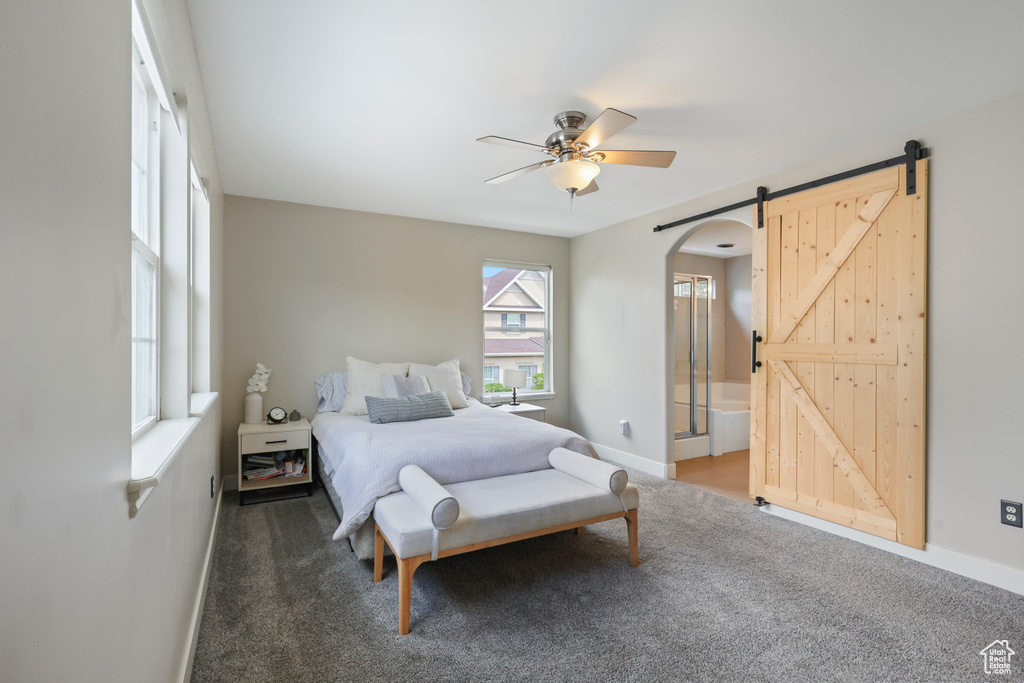 Carpeted bedroom featuring connected bathroom, ceiling fan, a barn door, arched walkways, and baseboards