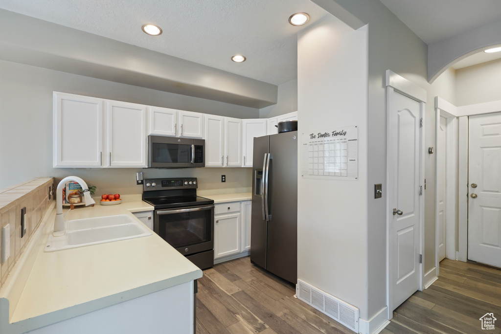 Kitchen featuring visible vents, dark wood-style floors, white cabinets, a sink, and appliances with stainless steel finishes