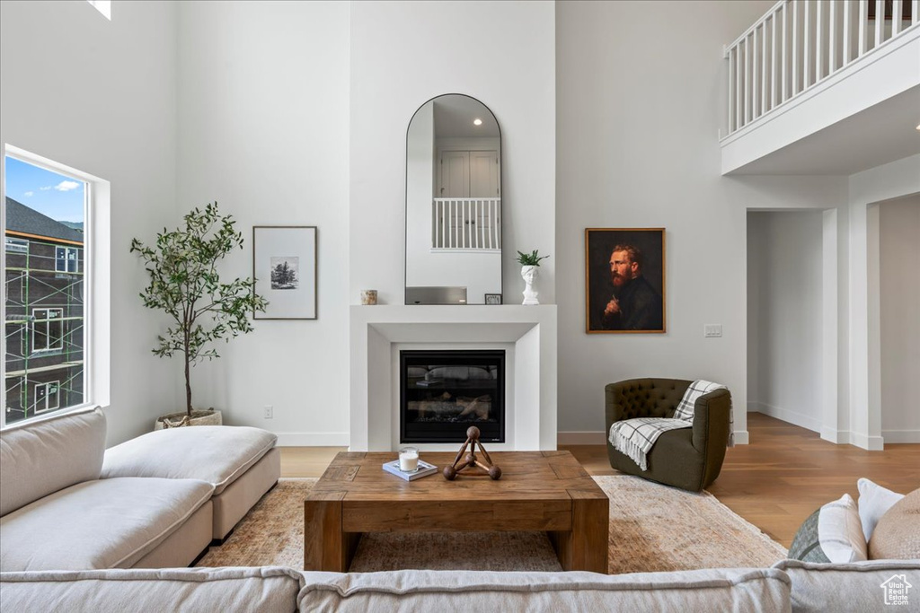 Living area featuring baseboards, a glass covered fireplace, wood finished floors, and a towering ceiling