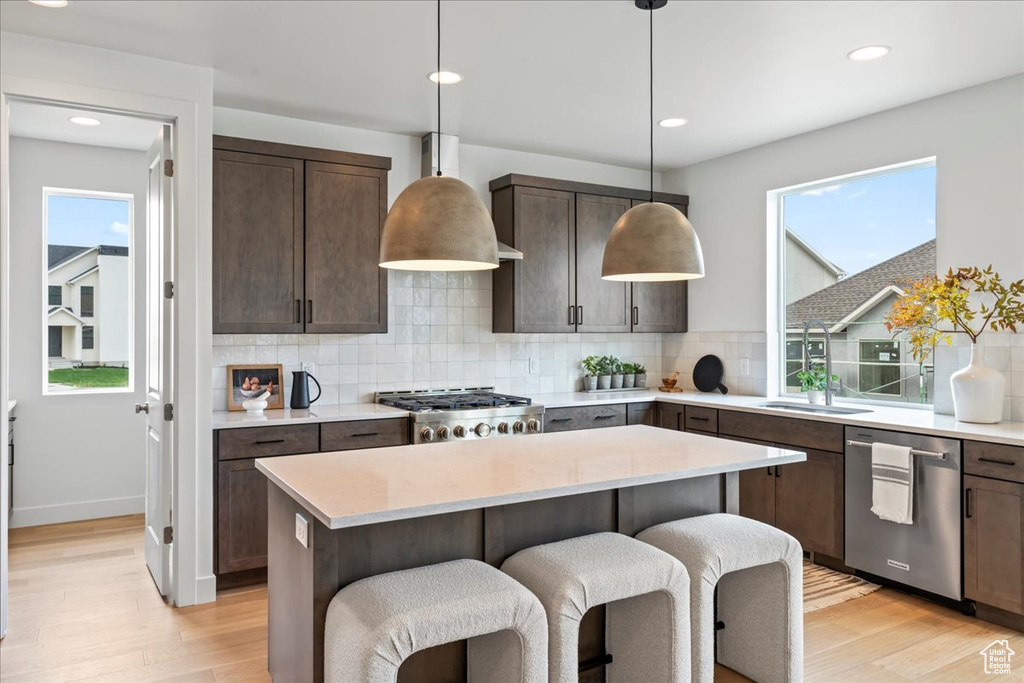 Kitchen featuring dark brown cabinets, light wood finished floors, dishwasher, decorative backsplash, and a kitchen island