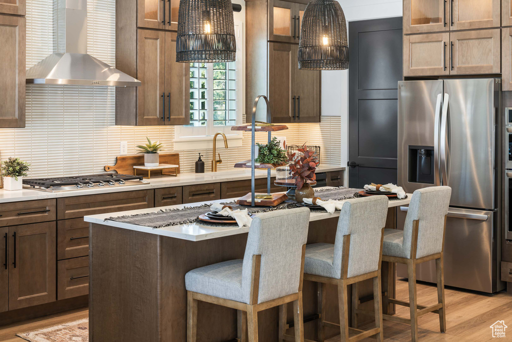 Kitchen featuring wall chimney range hood, glass insert cabinets, backsplash, and stainless steel appliances