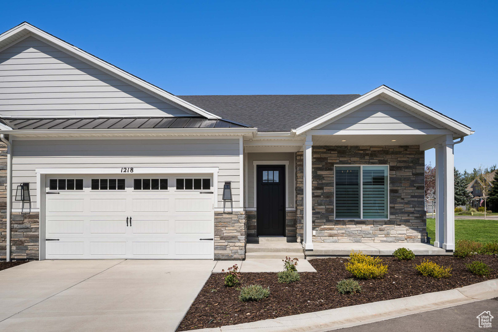 Craftsman-style house featuring an attached garage, driveway, stone siding, and a standing seam roof