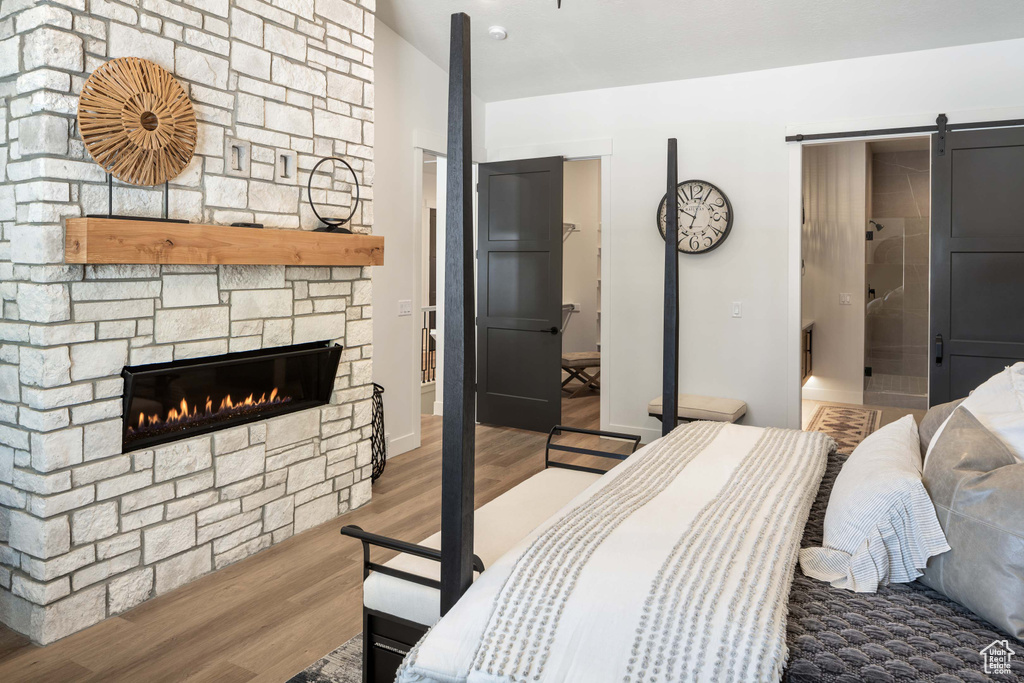 Bedroom featuring a stone fireplace, a barn door, and wood finished floors