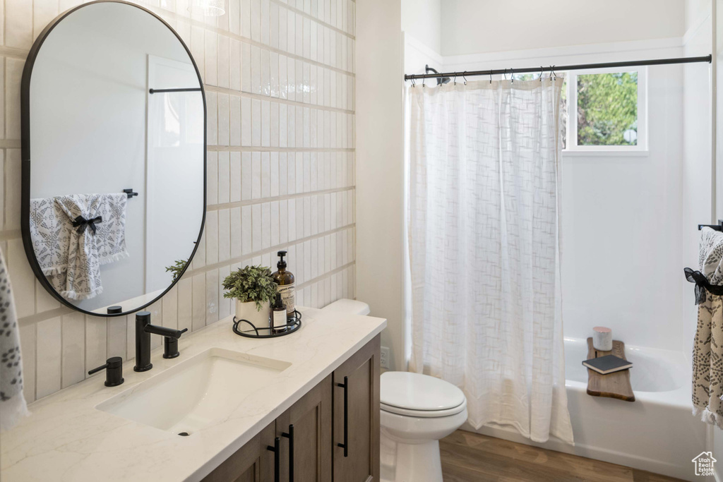 Bathroom with vanity, shower / tub combo with curtain, toilet, decorative backsplash, and wood finished floors