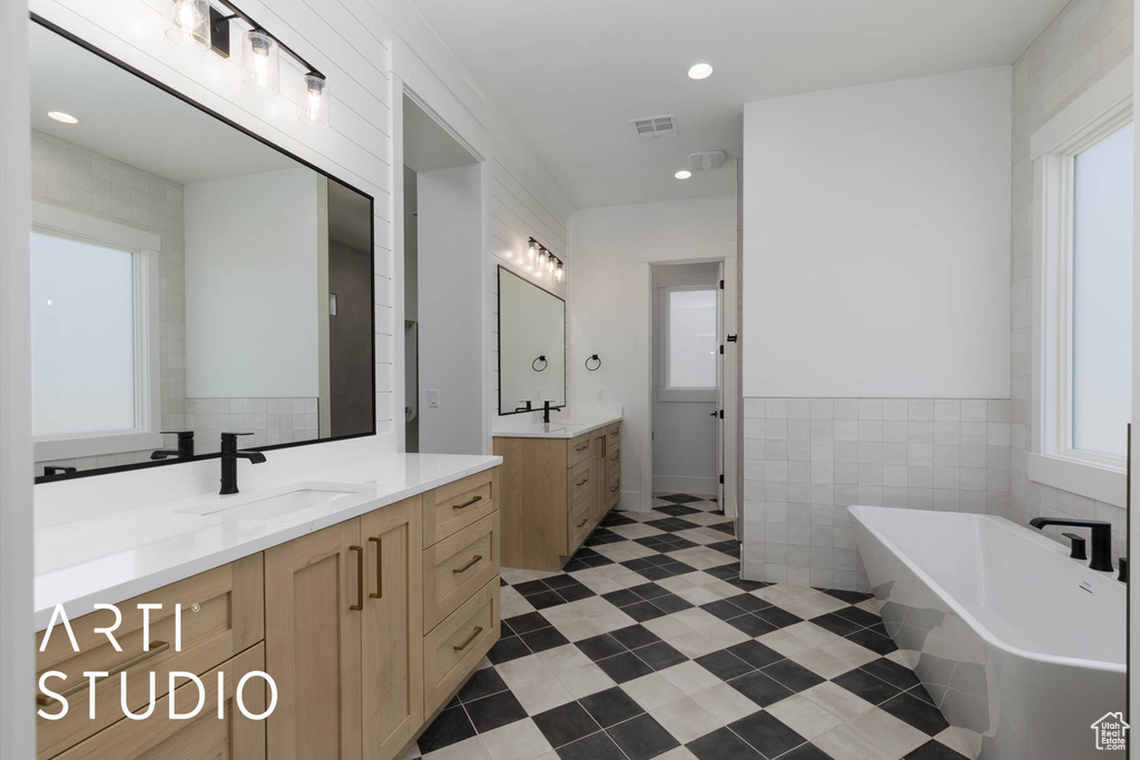 Bathroom featuring a freestanding tub, tile walls, two vanities, and tile patterned flooring