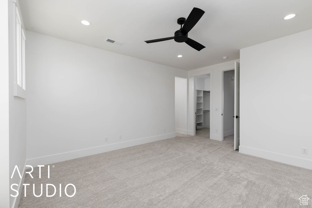Unfurnished bedroom with light carpet, baseboards, a walk in closet, recessed lighting, and a ceiling fan