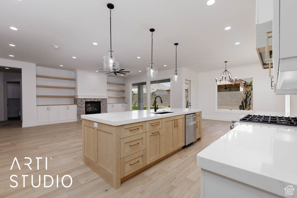 Kitchen with light brown cabinets, dishwasher, a sink, a glass covered fireplace, and light wood finished floors