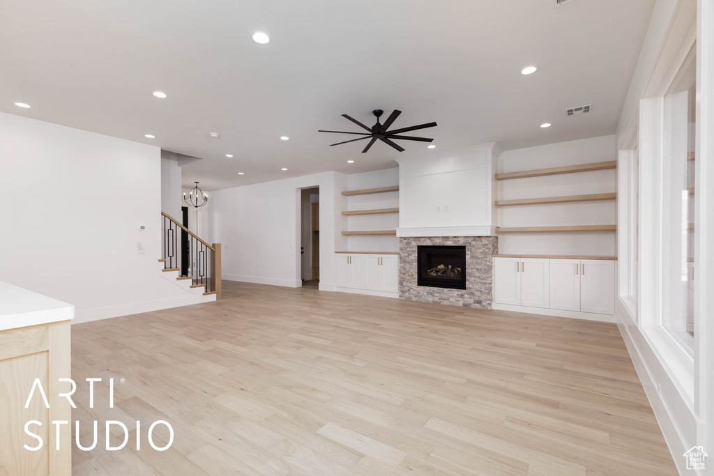 Unfurnished living room featuring recessed lighting, light wood-type flooring, a ceiling fan, a fireplace, and a chandelier