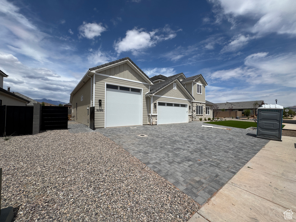 View of front of home featuring fence, stone siding, decorative driveway, board and batten siding, and an attached garage
