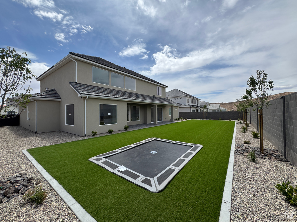 Rear view of property with a tiled roof, a trampoline, a fenced backyard, a yard, and stucco siding