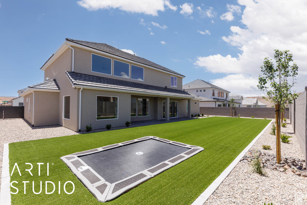 Rear view of house featuring a trampoline, stucco siding, and a patio area
