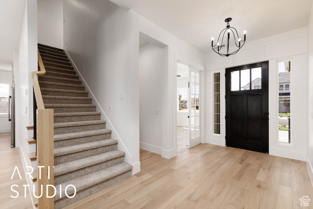 Entrance foyer with light wood-type flooring, stairs, a chandelier, and baseboards