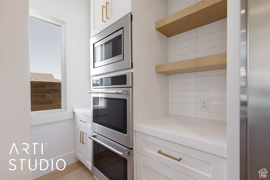 Kitchen with appliances with stainless steel finishes, decorative backsplash, light countertops, white cabinets, and open shelves