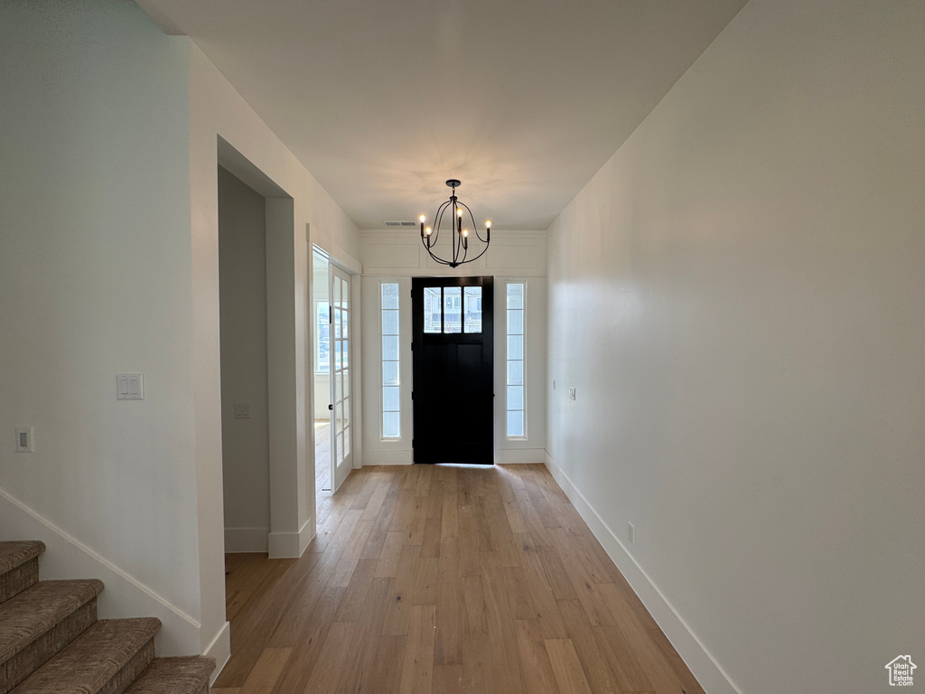 Entrance foyer with an inviting chandelier, baseboards, light wood finished floors, and stairs