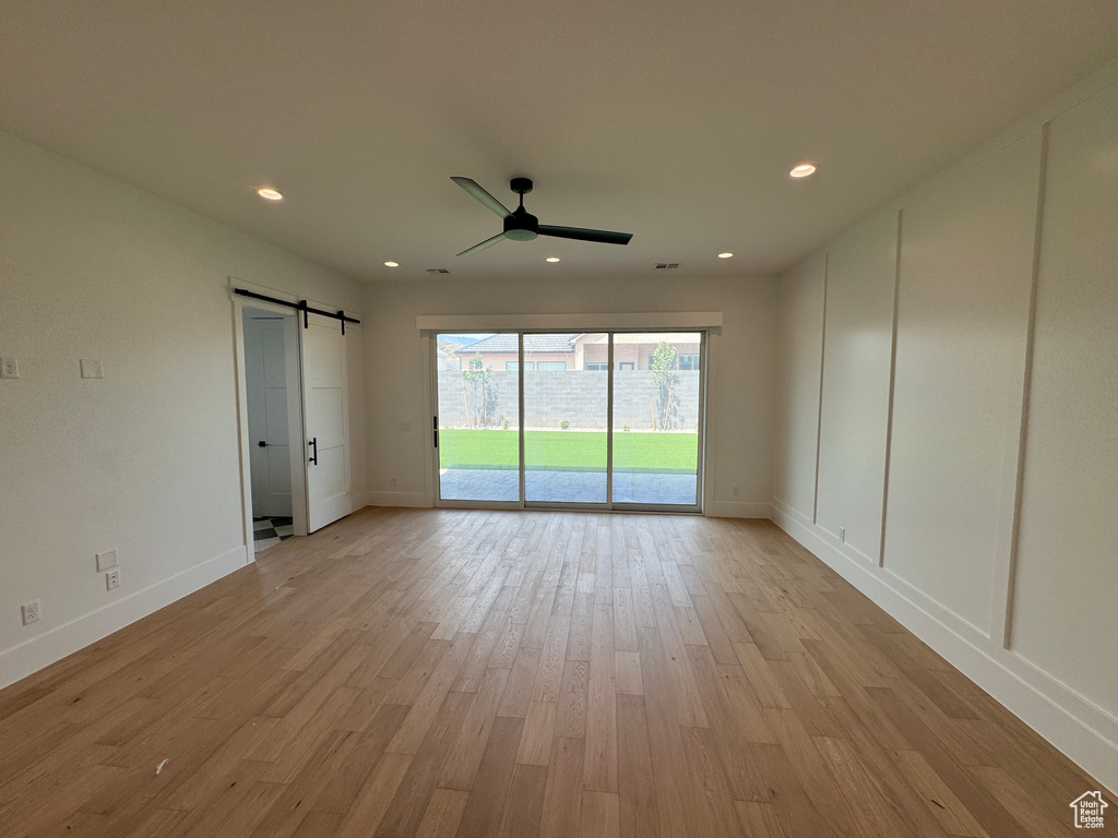 Empty room with baseboards, ceiling fan, light wood-type flooring, and a barn door