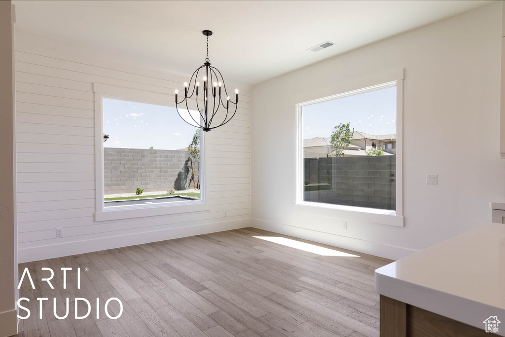 Unfurnished dining area with wood finished floors, a chandelier, and baseboards