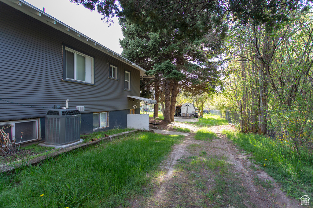 View of yard featuring dirt driveway, central AC, and fence