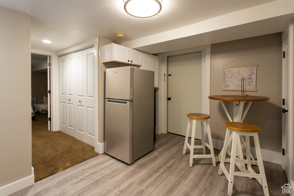 Kitchen featuring baseboards, freestanding refrigerator, light wood-type flooring, and white cabinetry